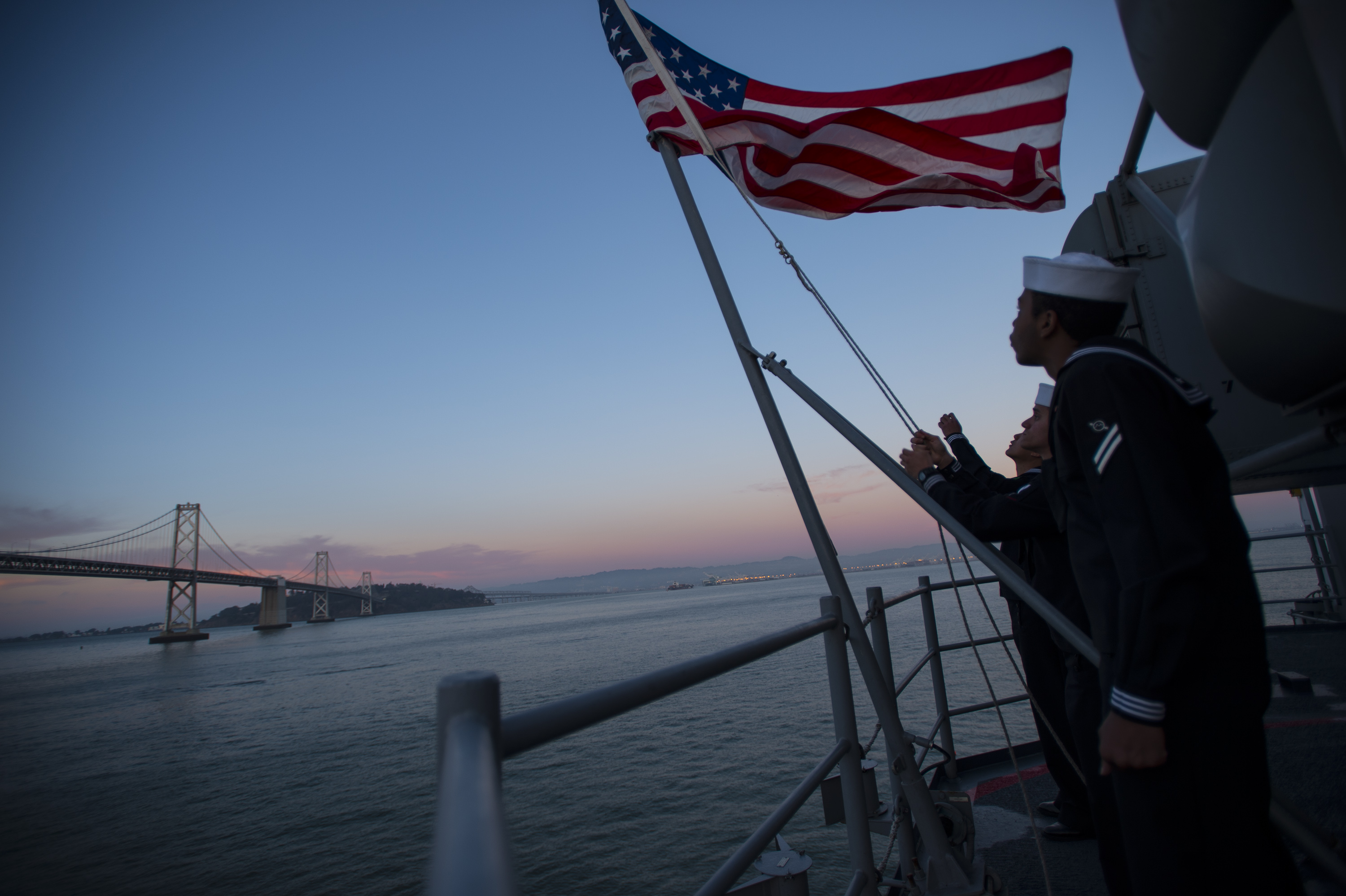 ailors assigned to the future amphibious assault ship USS America (LHA 6) perform evening colors on the ship's fantail while moored in San Francisco Bay. US Navy Photo