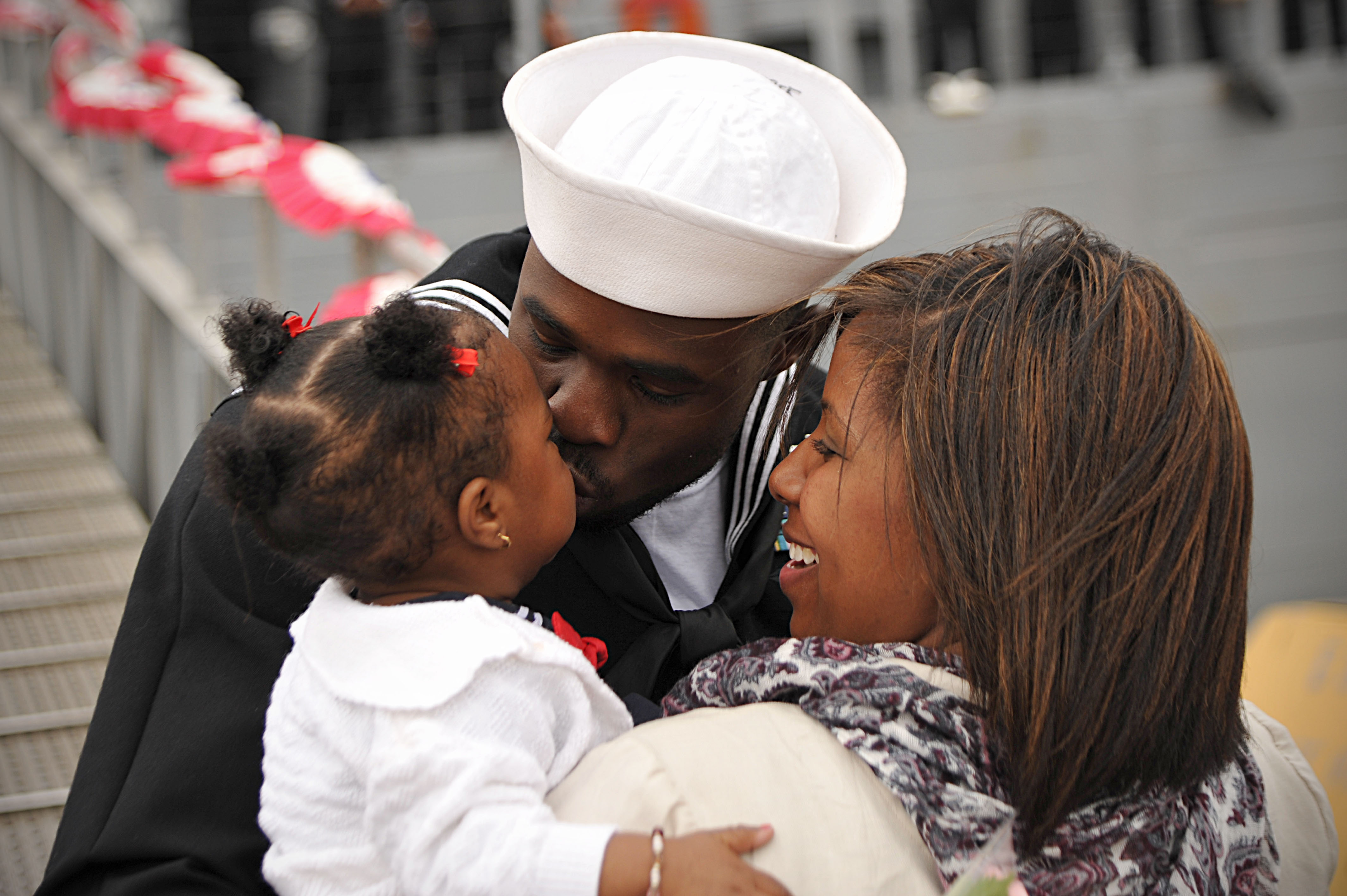 Boatswain's Mate 2nd Class Deshawn Byers kisses his daughter during a homecoming celebration for USS De Wert's (FFG-45). US Navy Photo