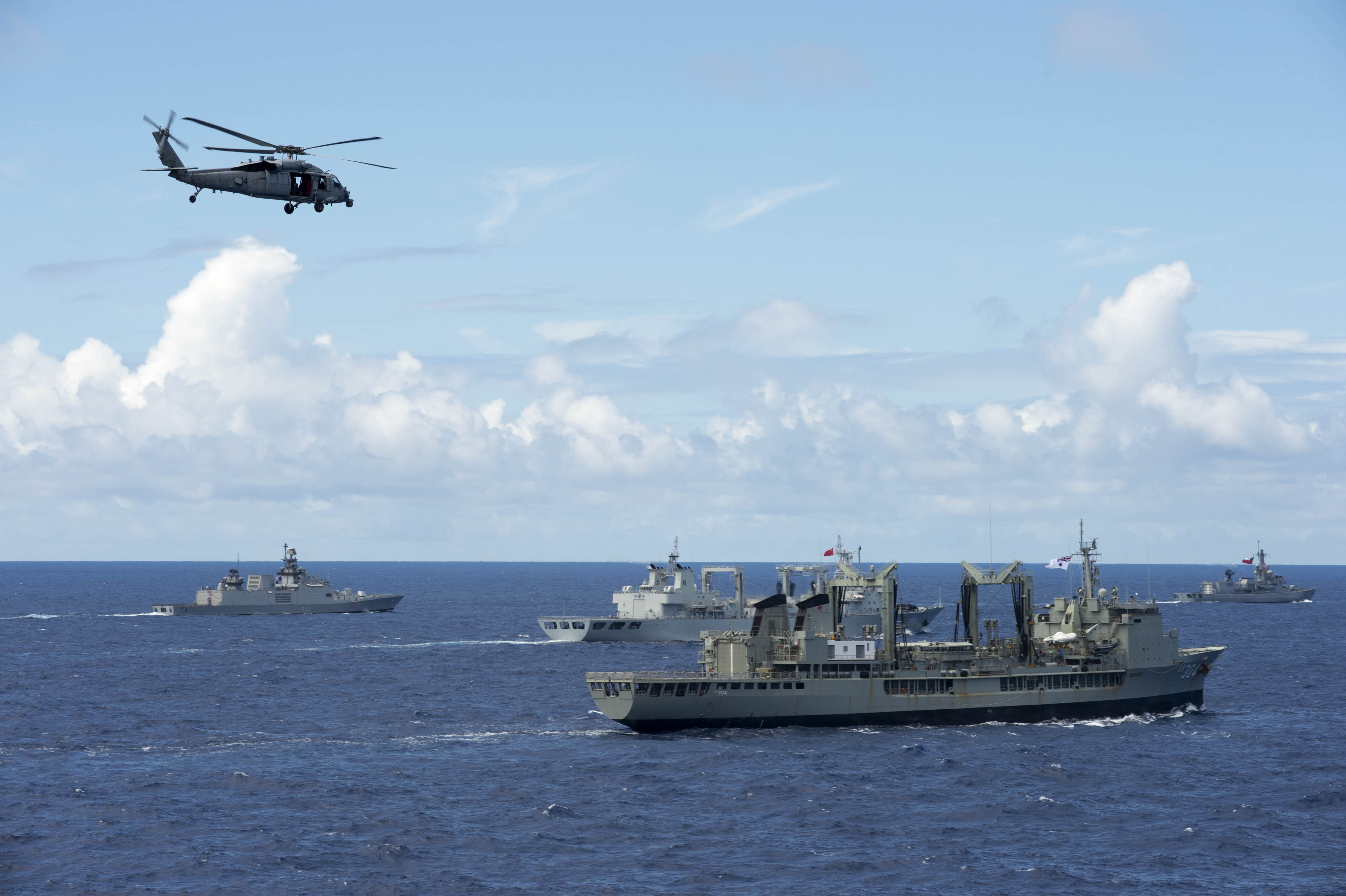 An MH-60S Sea Hawk helicopter assigned to Helicopter Sea Combat Squadron (HSC) 4 flies over several countries' ships in formation during a photo exercise for Rim of the Pacific (RIMPAC) Exercise 2014. US Navy photo.