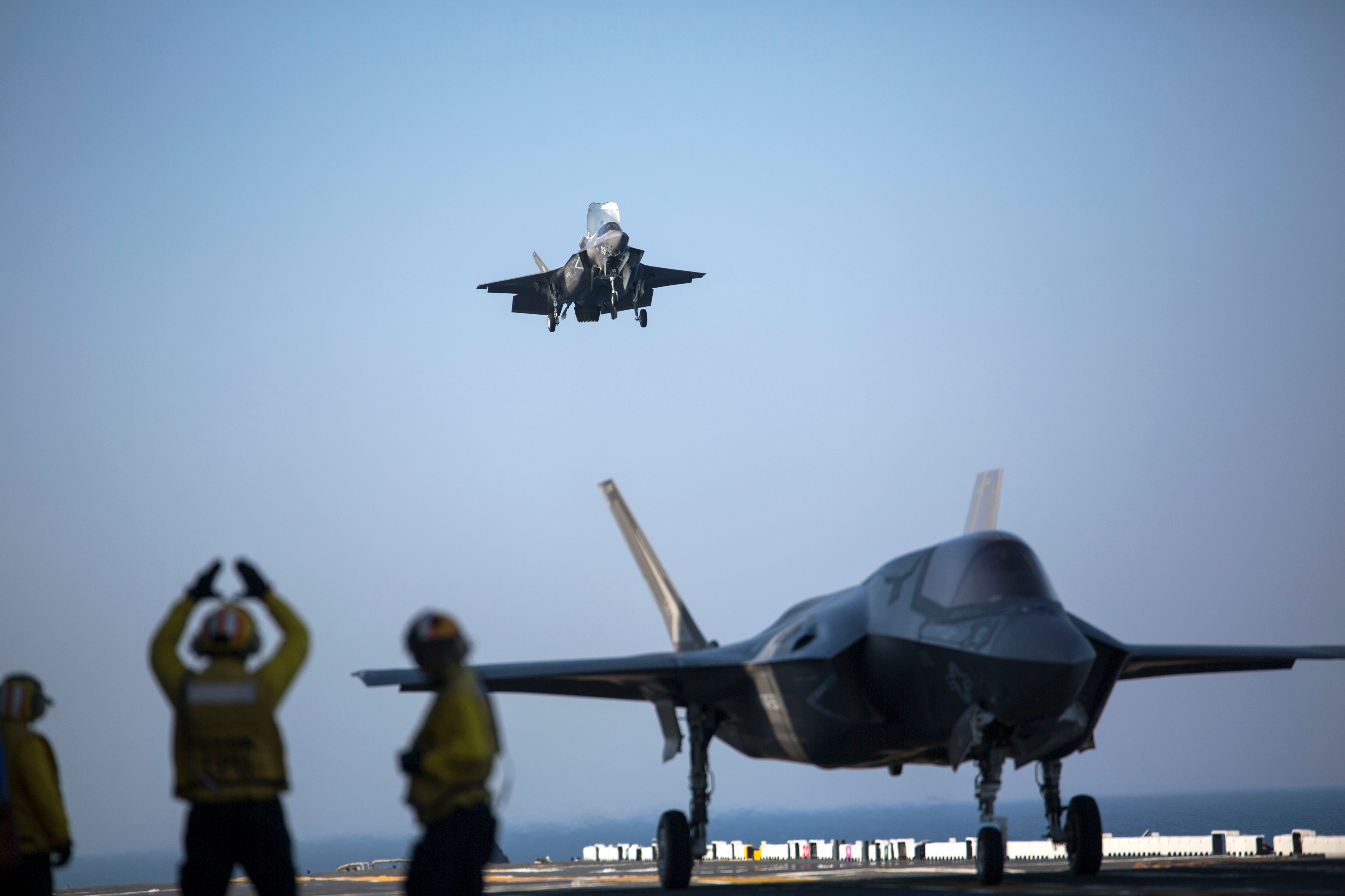 A sailor aboard the USS Wasp (LHD-1) signals to the pilot of an F-35B Lightning II Joint Strike Fighter to land as it arrives for the first phase of operational testing, May 18, 2015. US Marine Corps photo.
