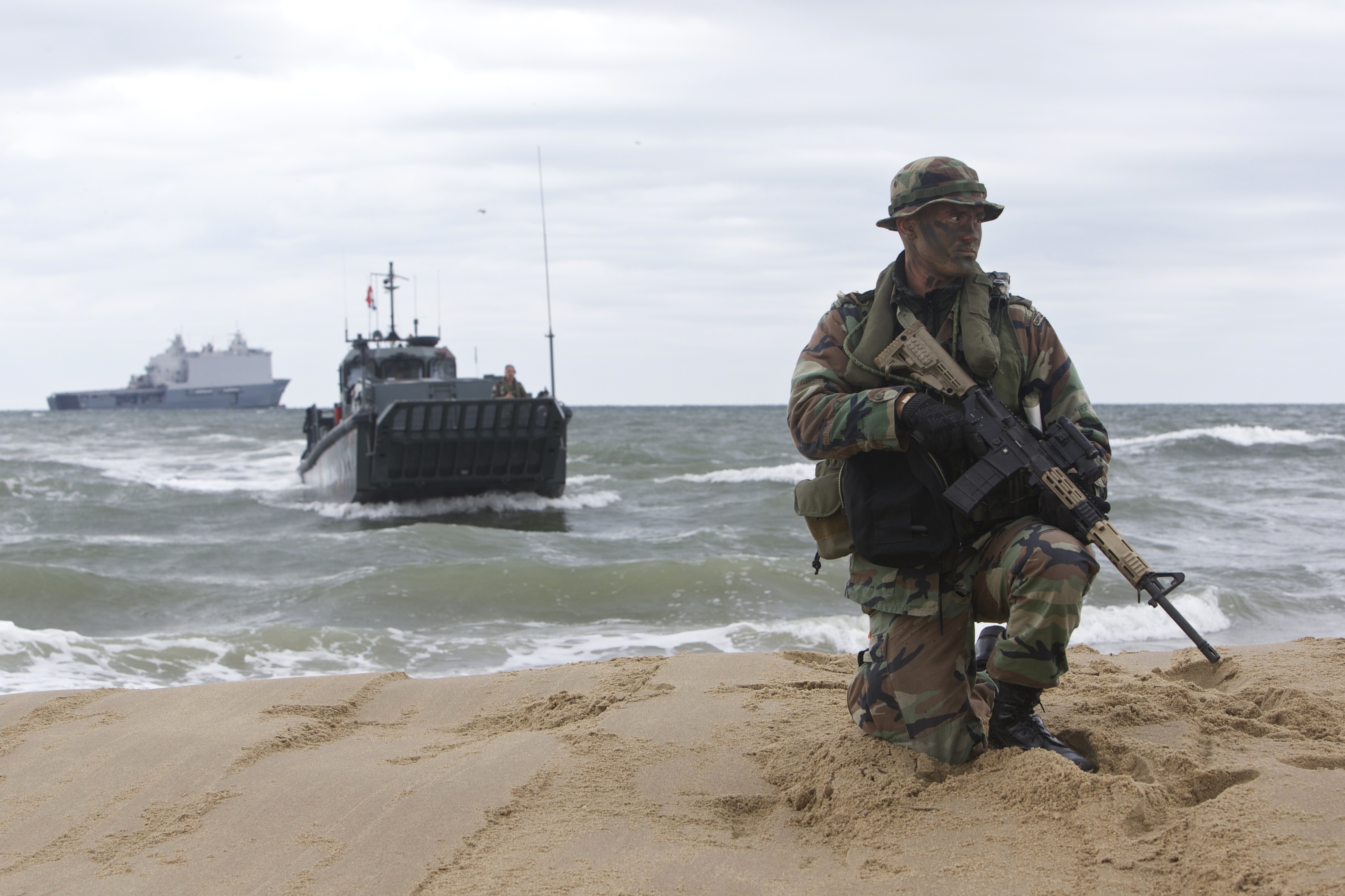 A Dutch marine from the Royal Netherlands Marine Corps is securing the area of Utah Beach during Bold Alligator 14. Dutch amphibious ship HNLMS Johan de Witt (L-801), in the background, served as the command and control headquarters during the exercise to improve interoperability between Dutch, American and other partners' militaries. US Navy photo courtesy of the Royal Netherlands Air Force.