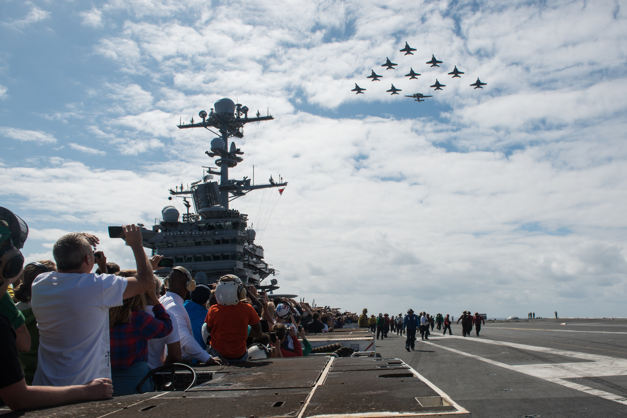 Sailors, family and friends watch as aircraft from Carrier Air Wing (CVW) 9 fly in formation above USS John C. Stennis (CVN 74) during an air power demonstration on Aug. 7, 2016, during the tiger cruise, which is an opportunity for Sailors to invite their family and friends to experience life underway aboard a Navy ship. US Navy photo.