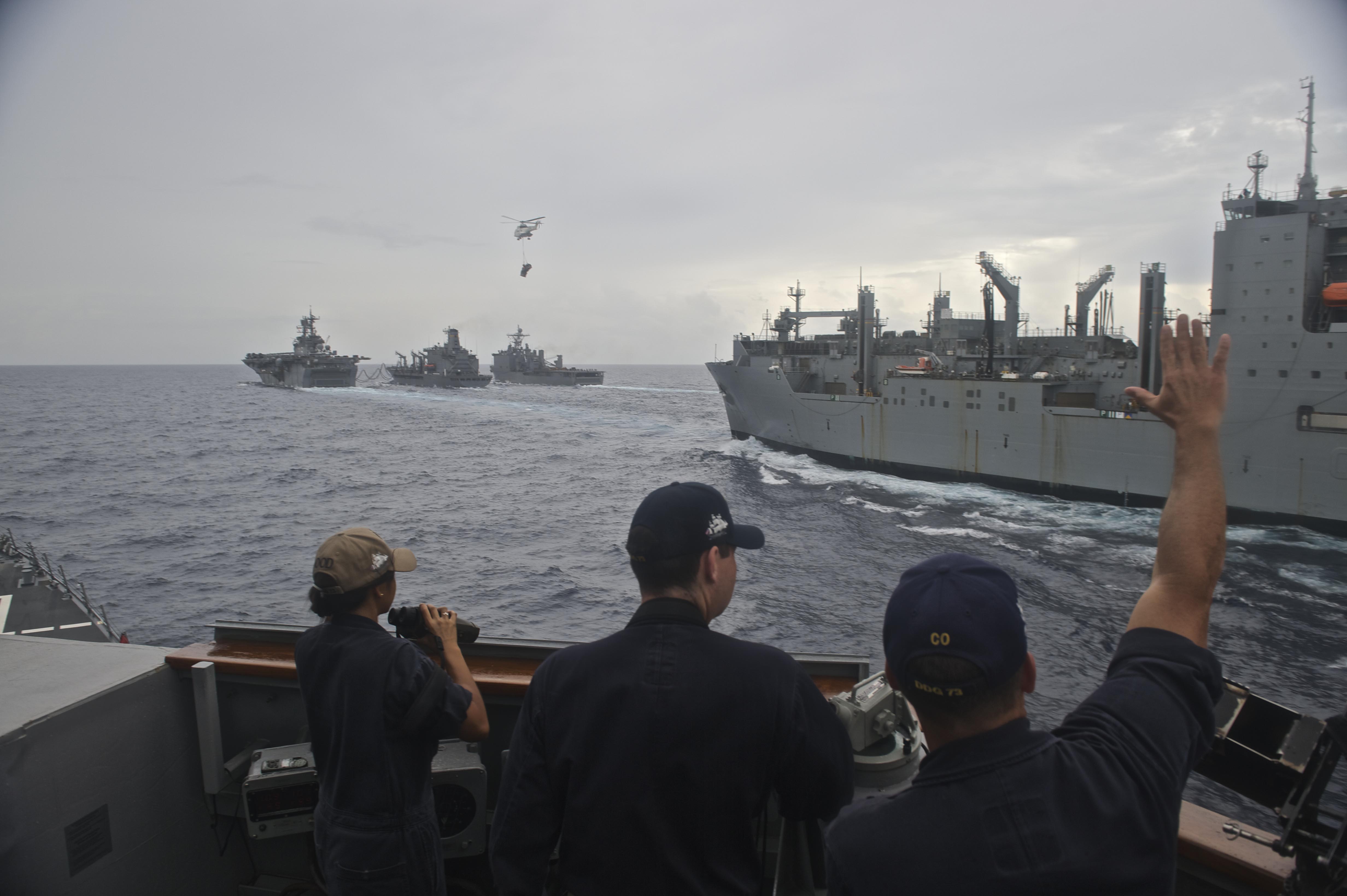 Cmdr. Garrett Miller, commanding officer of the guided-missile destroyer USS Decatur (DDG 73) greets the Military Sealift Command dry cargo and ammunition ship USNS Washington Chambers (T-AKE 11) as it conducts a replenishment-at-sea with the Bonhomme Richard Expeditionary Strike Group (BHR ESG) as part of interoperability drills between the Pacific Surface Action Group (PAC SAG) and BHR ESG. The drills are meant to enhance readiness of cruiser-destroyer ships to rapidly integrate with an amphibious task force to provide increased capability for amphibious operations in support of crisis response or disaster relief. US Navy photo.