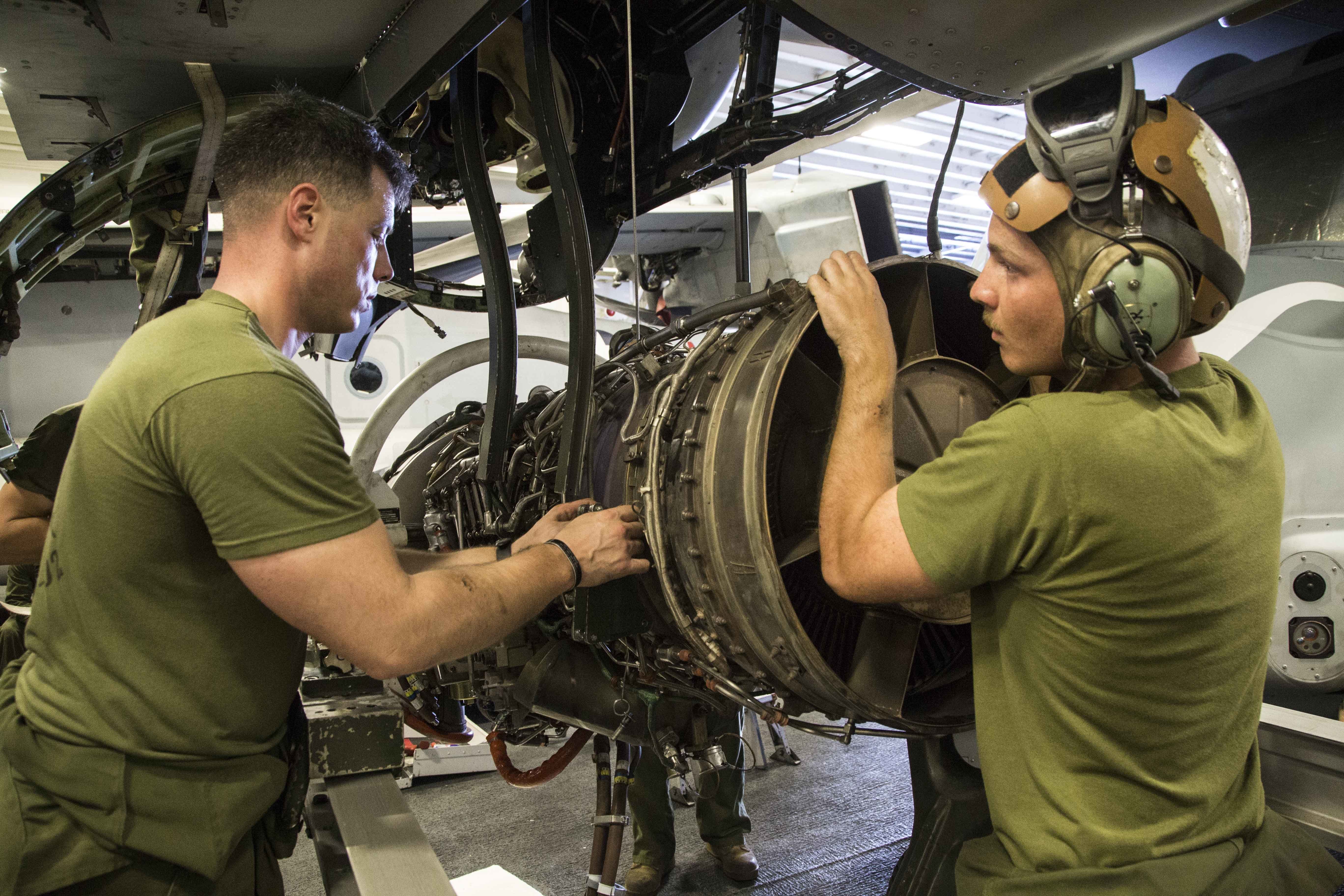 U.S. Marine Sgt. Ryan Boele (left), a MV-22 flight line mechanic chief with Marine Medium Tiltrotor Squadron 163 (Reinforced), 11th Marine Expeditionary Unit, and Lance Cpl. David Bath (right), a MV-22 flight line mechanic with VMM-163, 11th MEU, adjust cables on an engine of an MV-22 Osprey within the hanger bay of the USS Makin Island (LHD 8) Dec. 27. US Marine Corps photo.